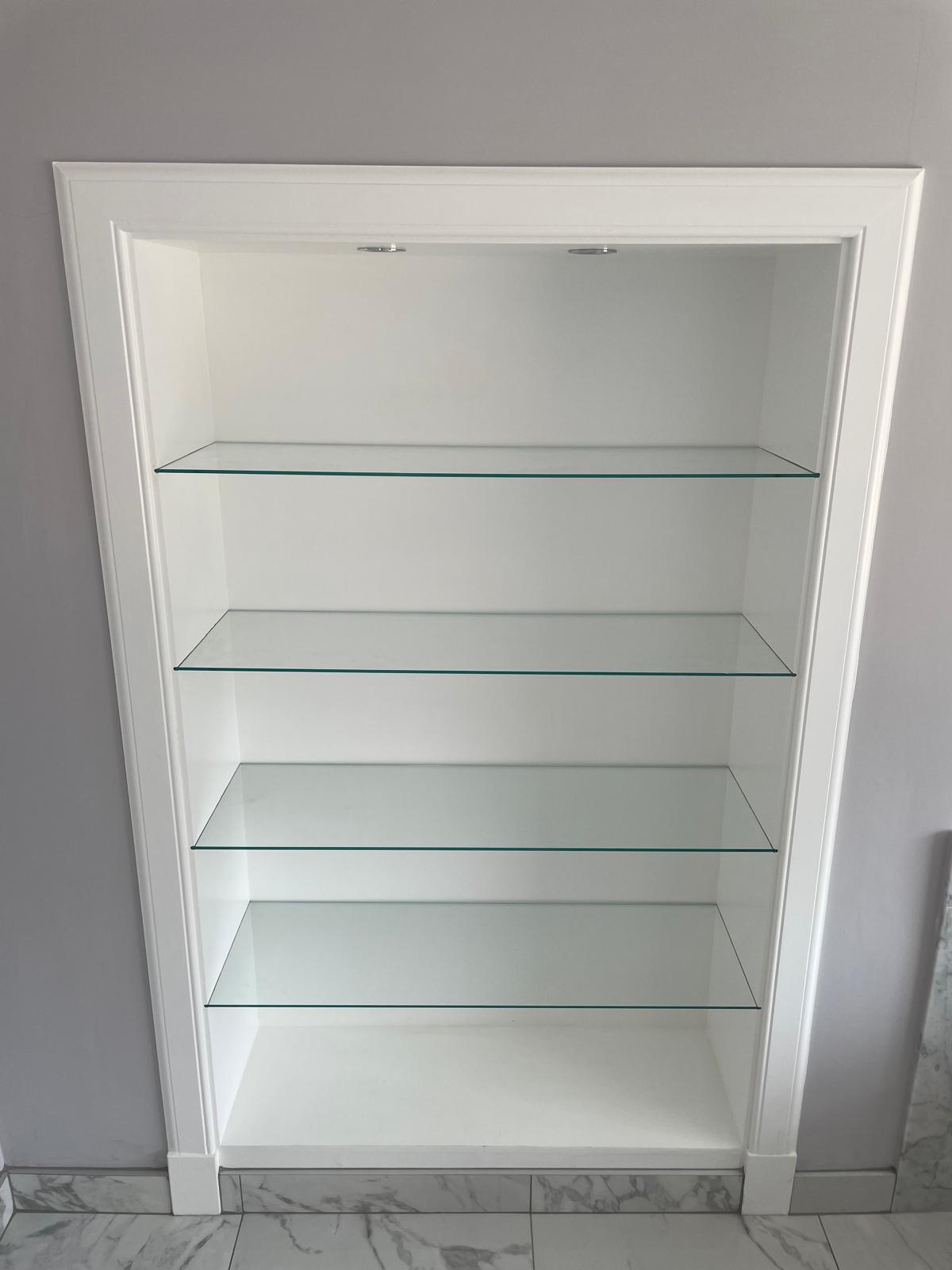 Fitted alcove unit with glass shelves, painted white, on marble-effect tiled floor.