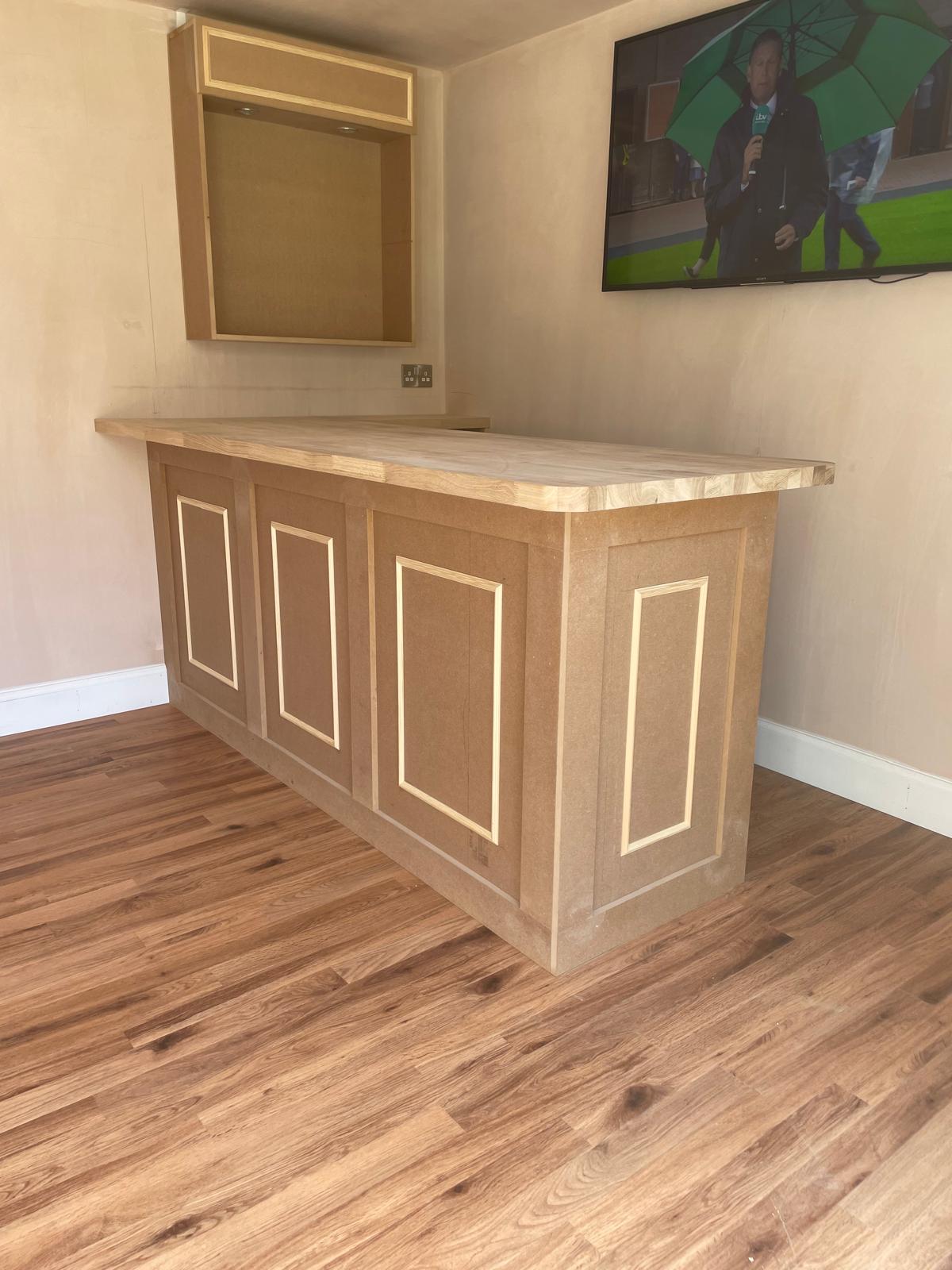 Bespoke panelled bar with wooden countertop inside a garden room.
